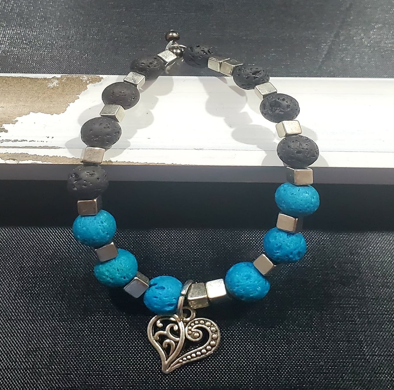 a bracelet of blue and black lava rocks with a metal heart pendant