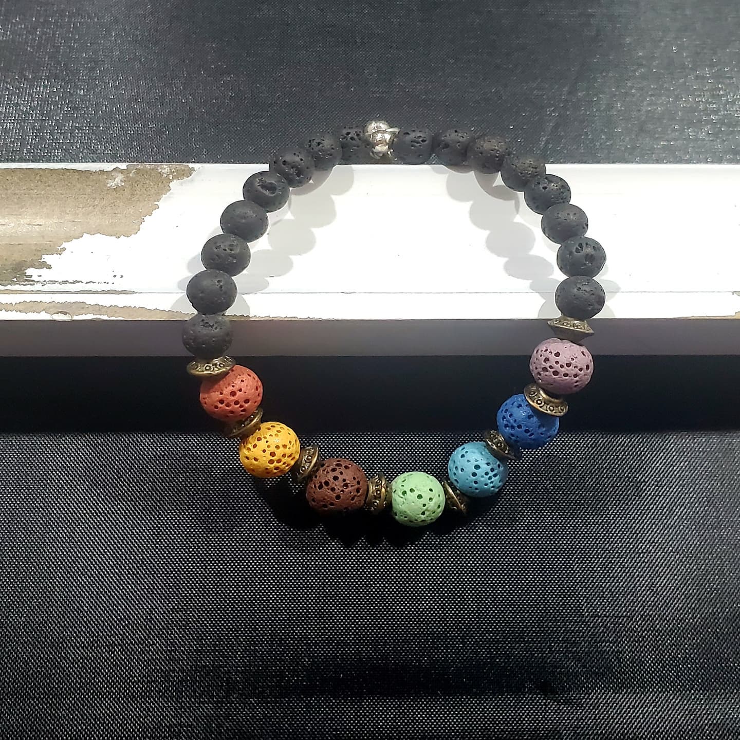 a bracelet of black lava rocks with a rainbow of lava rocks at the bottom