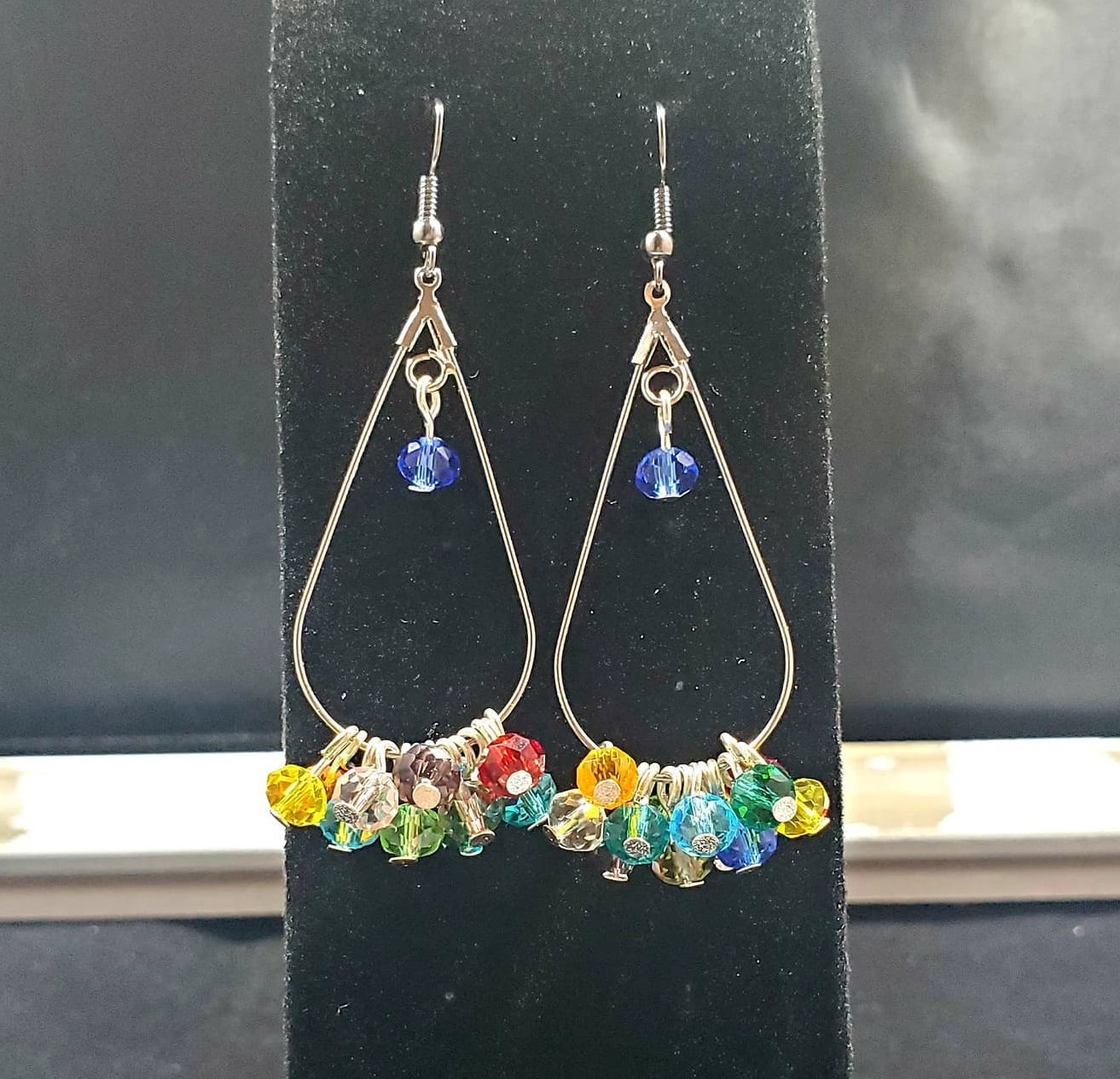 teardrop shaped earrings with a blue gem bead in the center and a rainbow of gem beads along the bottom
