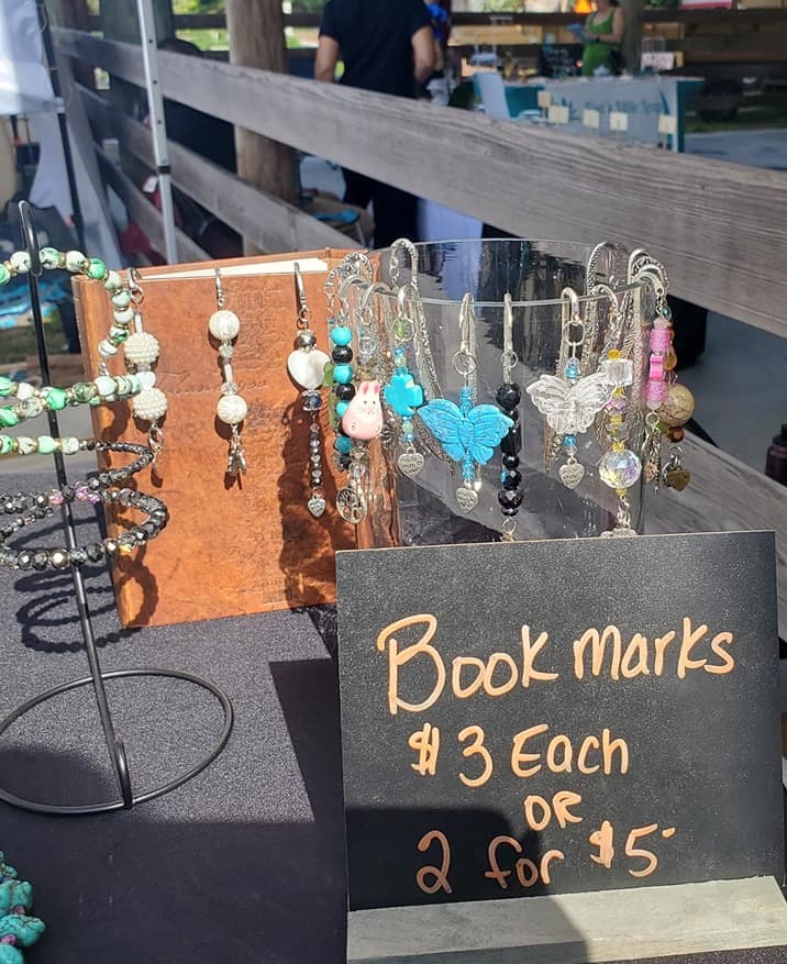 A display of beaded bookmarks with butterfly pendants next to a chalkboard sign advertising them